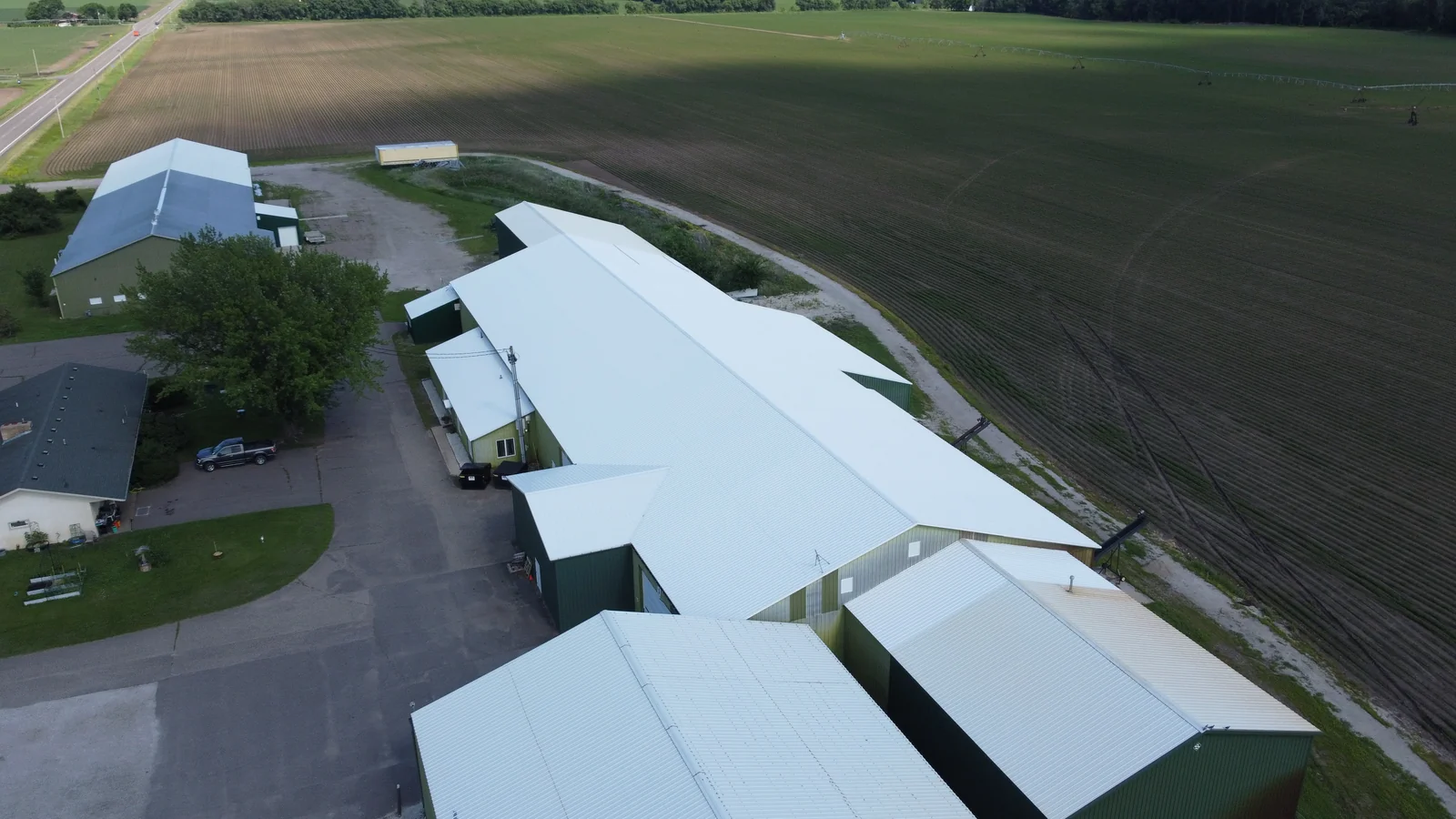 Drone shot of the metal-roofed farm building with green crop fields stretching to the horizon