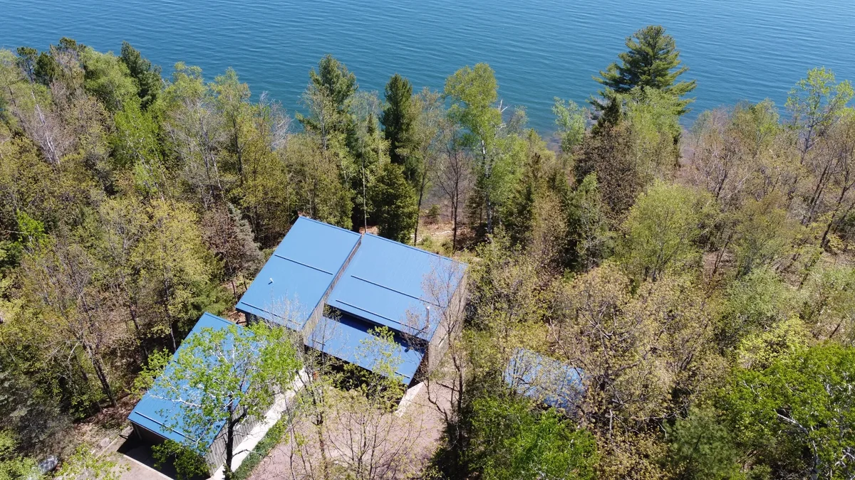 Bird's-eye view of the blue metal roof with the lake stretching beyond the treetops