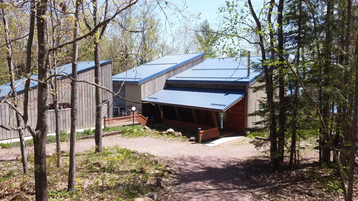 The blue-roofed home framed by tall trees on its wooded lot
