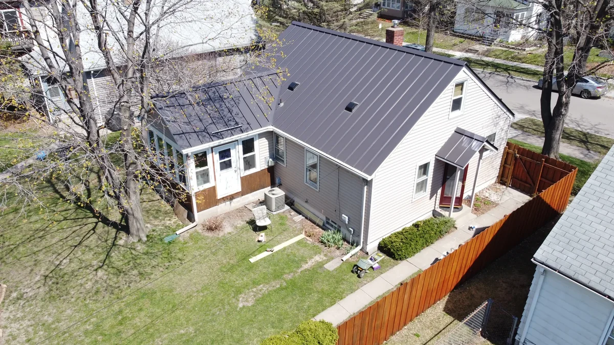 Rear and side view of the gray home showing the dark metal roof wrapping over the additions.