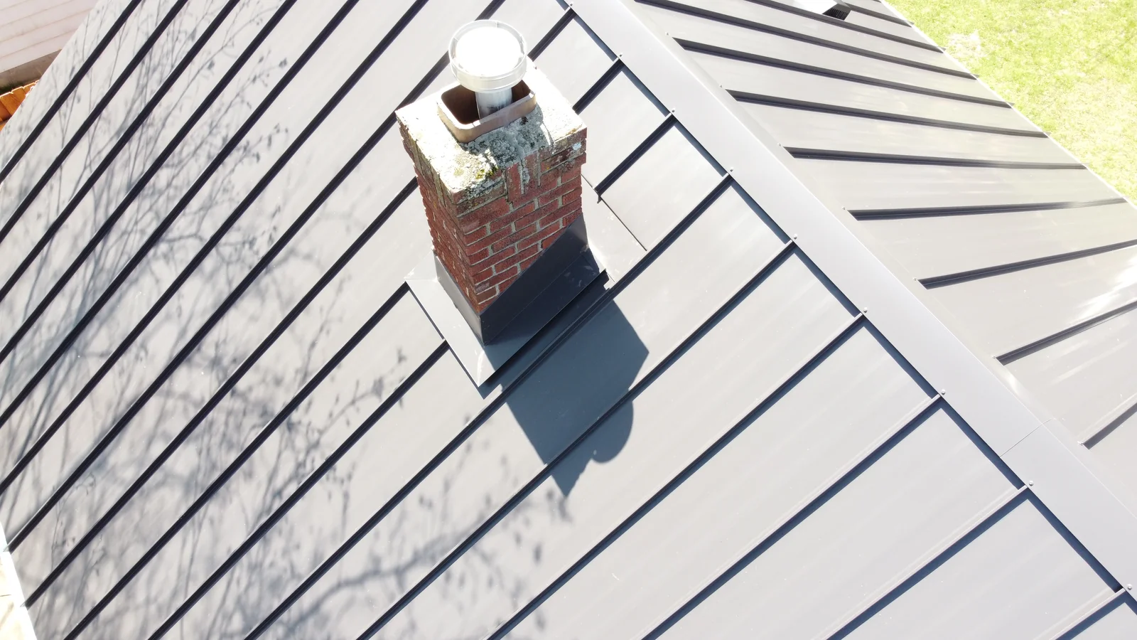 Close overhead look at the standing seam panels meeting a brick chimney and crisp roof ridges.