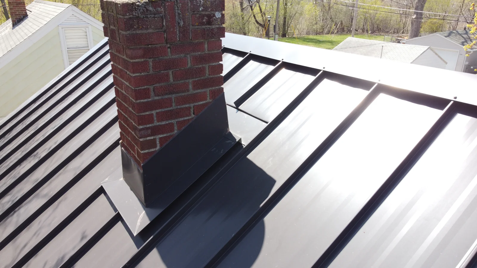 Detail of the metal roof seams running tight against the weathered brick chimney.