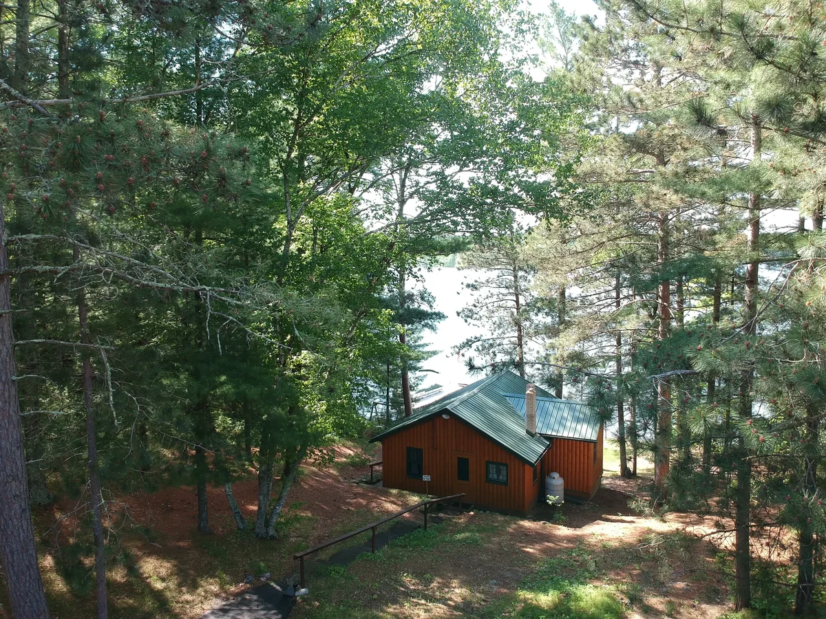 Drone shot of the green metal-roofed cabin framed by tall pines with the lake beyond