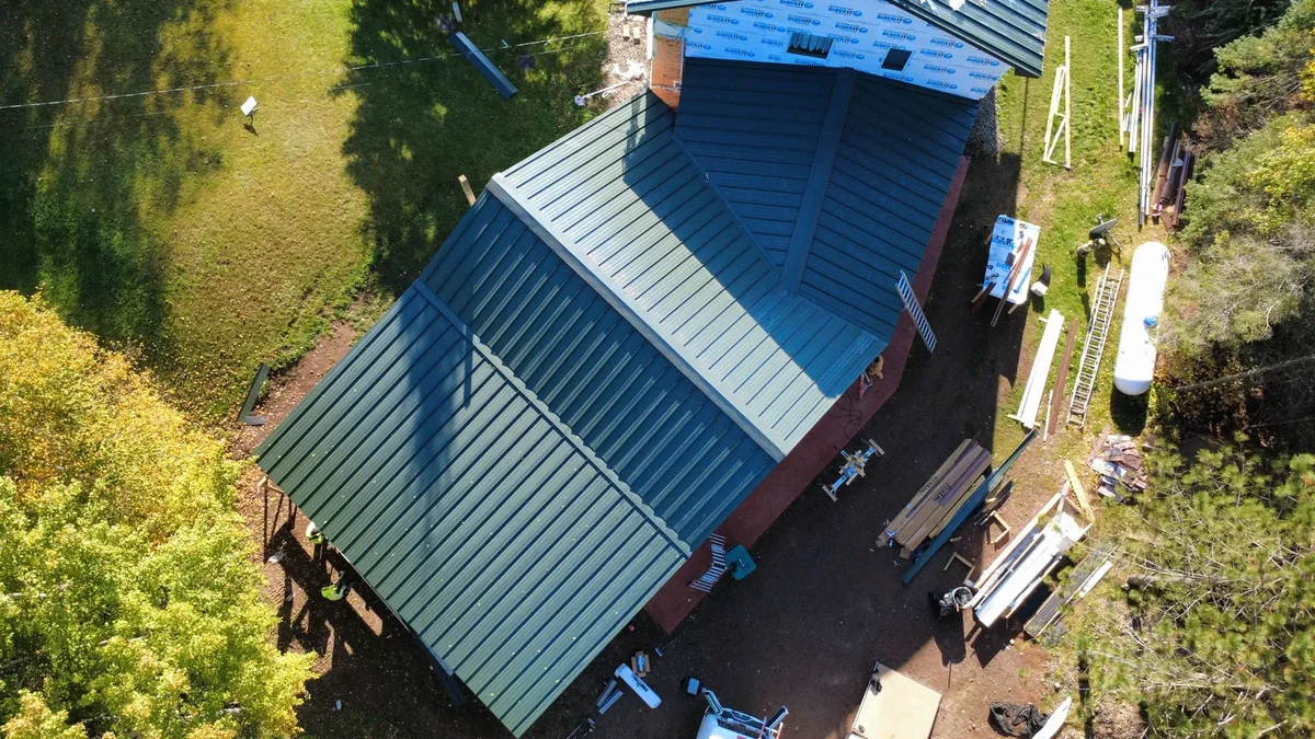 Steep blue metal roof on a forested cabin, its panels running cleanly down to the eaves.