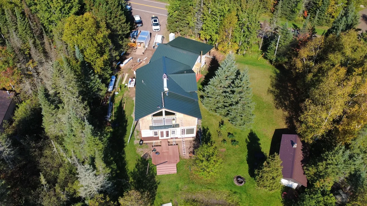 Drone shot of a multi-gabled home with a slate-blue metal roof tucked among tall pines.