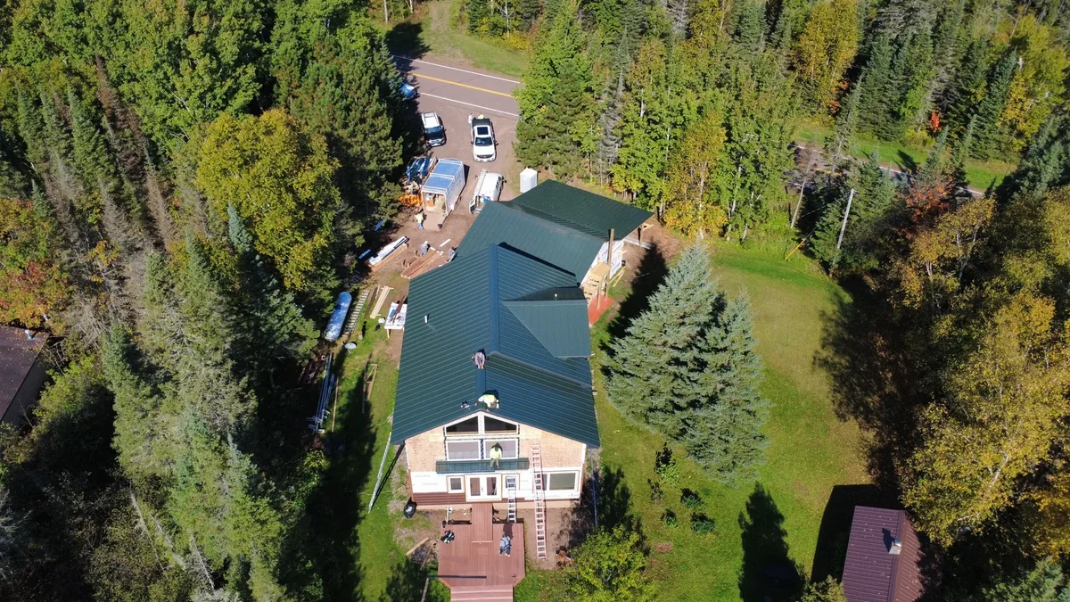 Wooded property with a blue-roofed cabin and a private dock leading into the water.