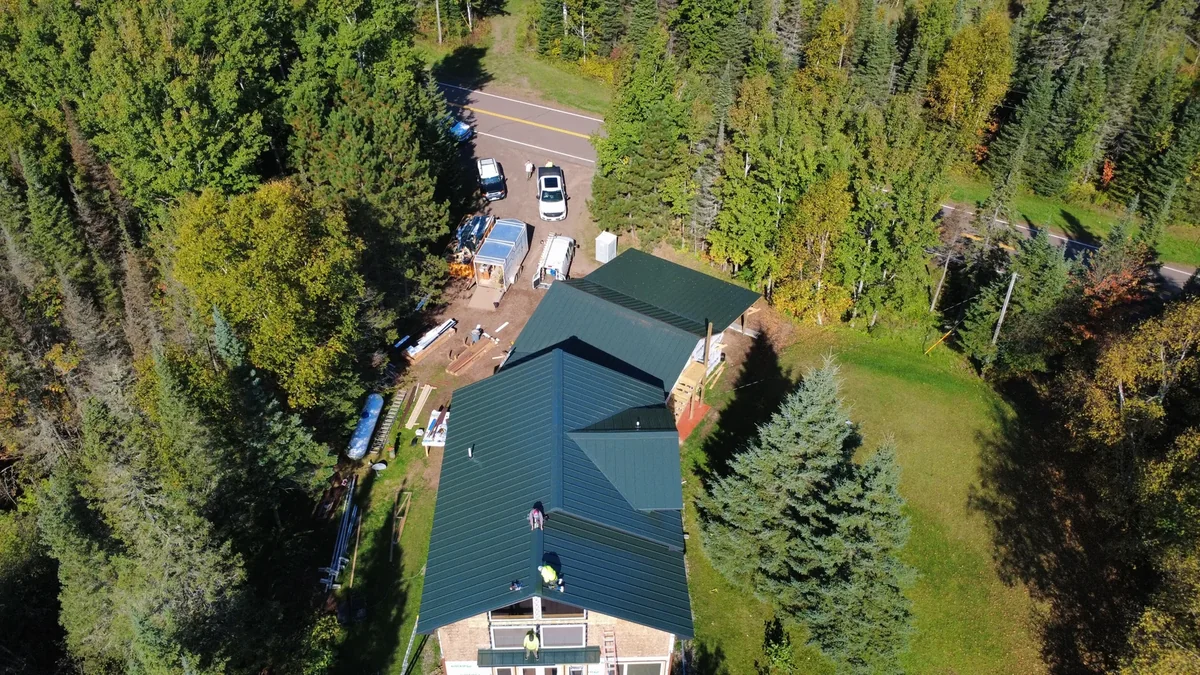 Side profile of the cabin's blue metal roof set against dense evergreen forest.