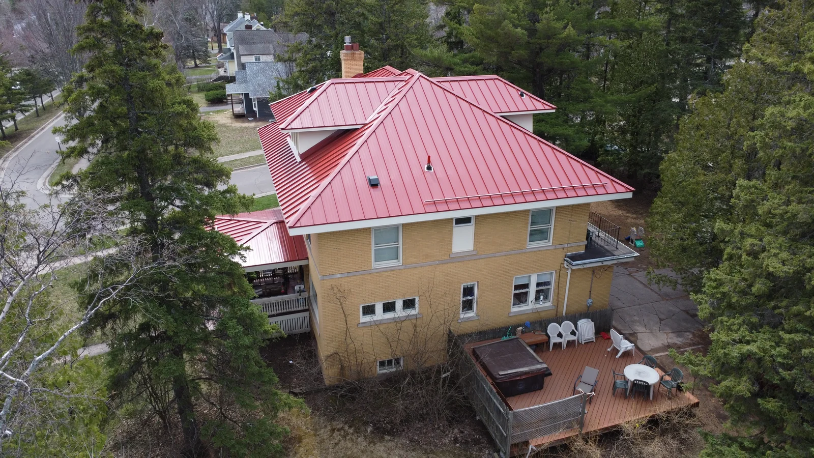 Rear-quarter aerial of the red metal roof showing the home's back deck and yard.
