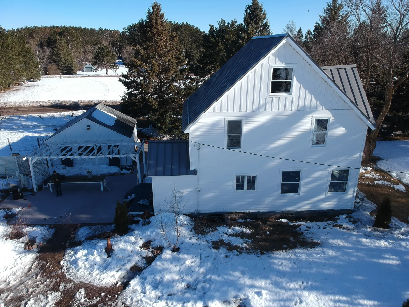 Snowy aerial view of a white two-story farmhouse capped with a slate-blue standing seam metal roof in Cloquet, MN.
