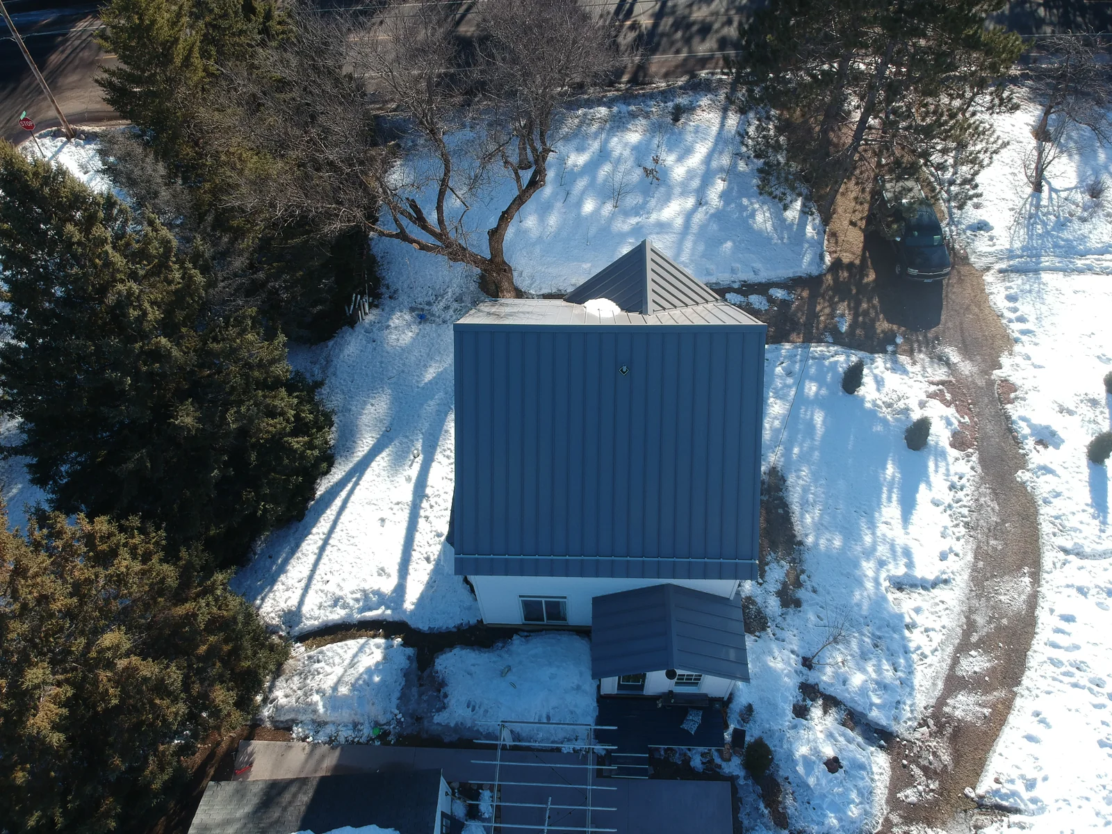 Overhead drone shot of the gabled metal roof surrounded by winter snow and bare trees.