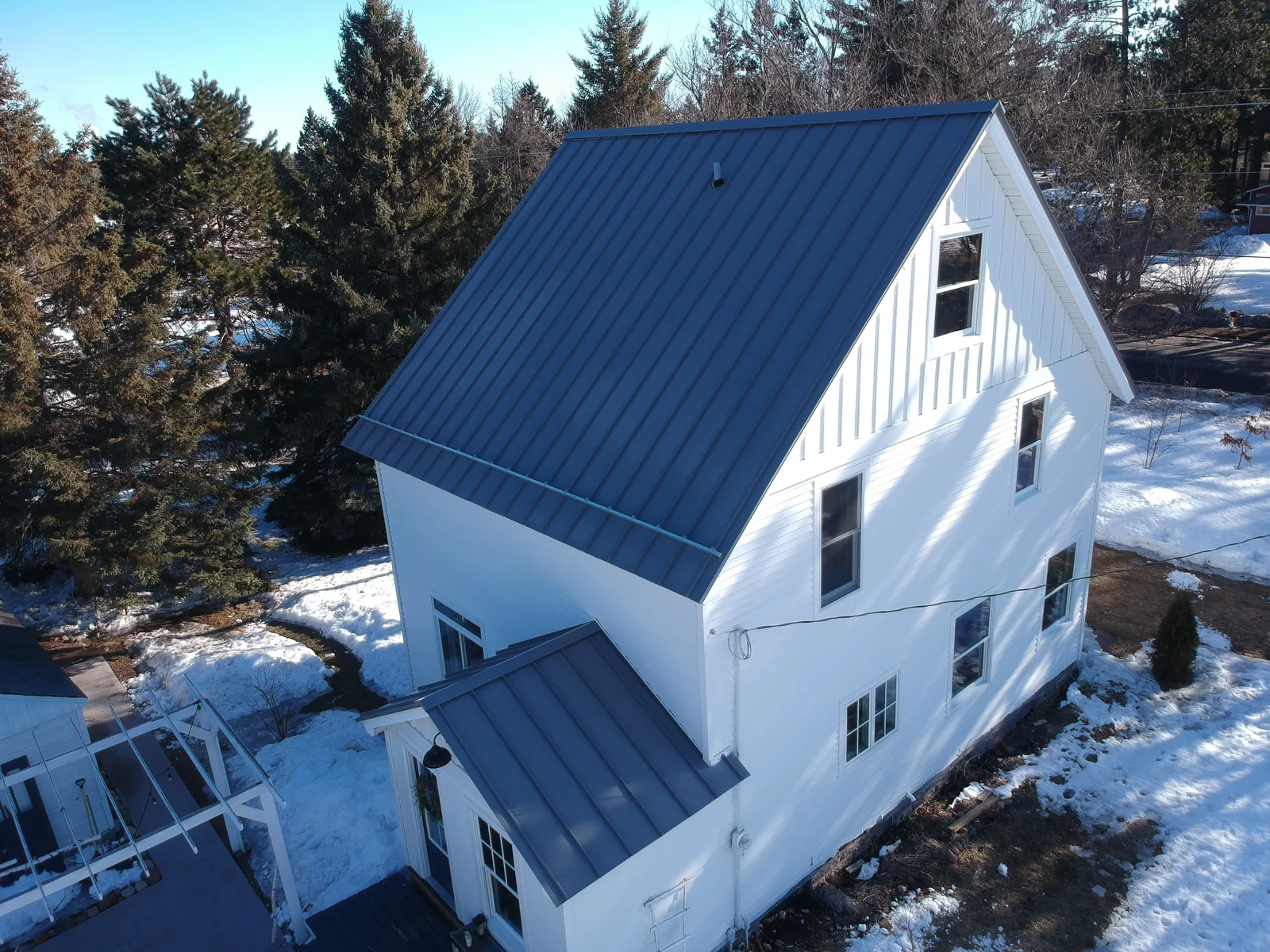 Side angle of the white home showing the steep blue metal roof and gable ends.
