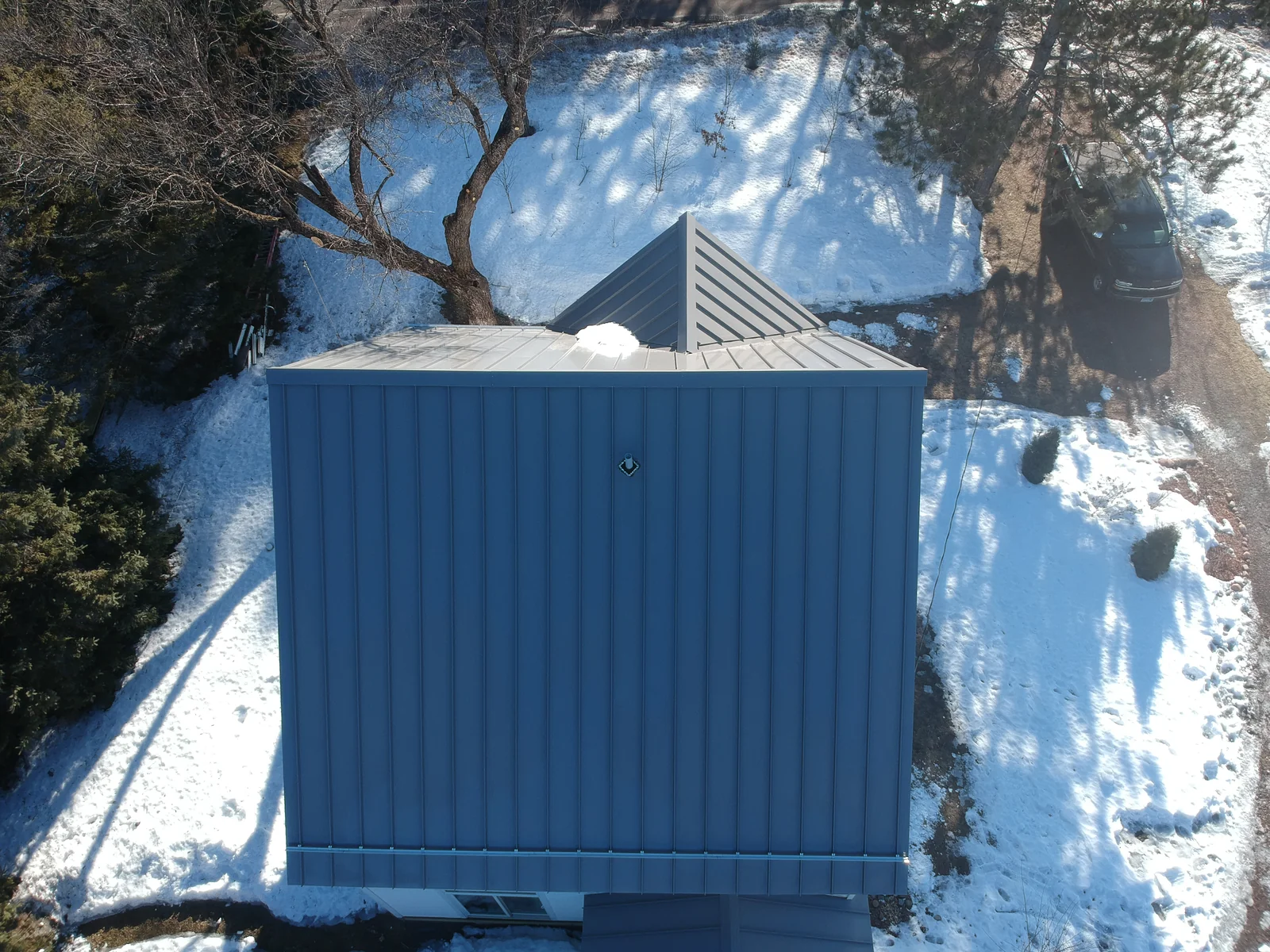 Near-overhead look at the hipped metal roof of the outbuilding beside the main house.