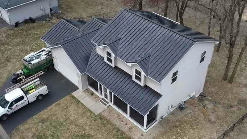 Drone shot of a gray standing seam roof on a white sided home with a work truck in the driveway