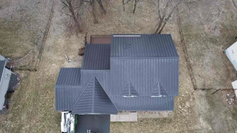 High aerial of the slate-gray metal roof set among bare trees and a winding street