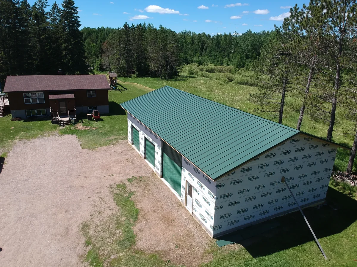 Aerial view of a green standing seam metal roof on a pole building near Cotton, MN, surrounded by woods and gravel drive.