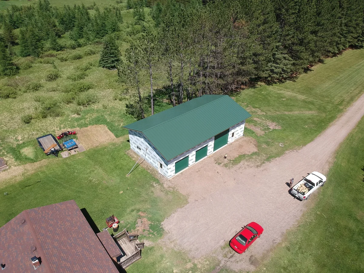 Wide shot of the green-roofed building in its forest clearing with a parked vehicle nearby.