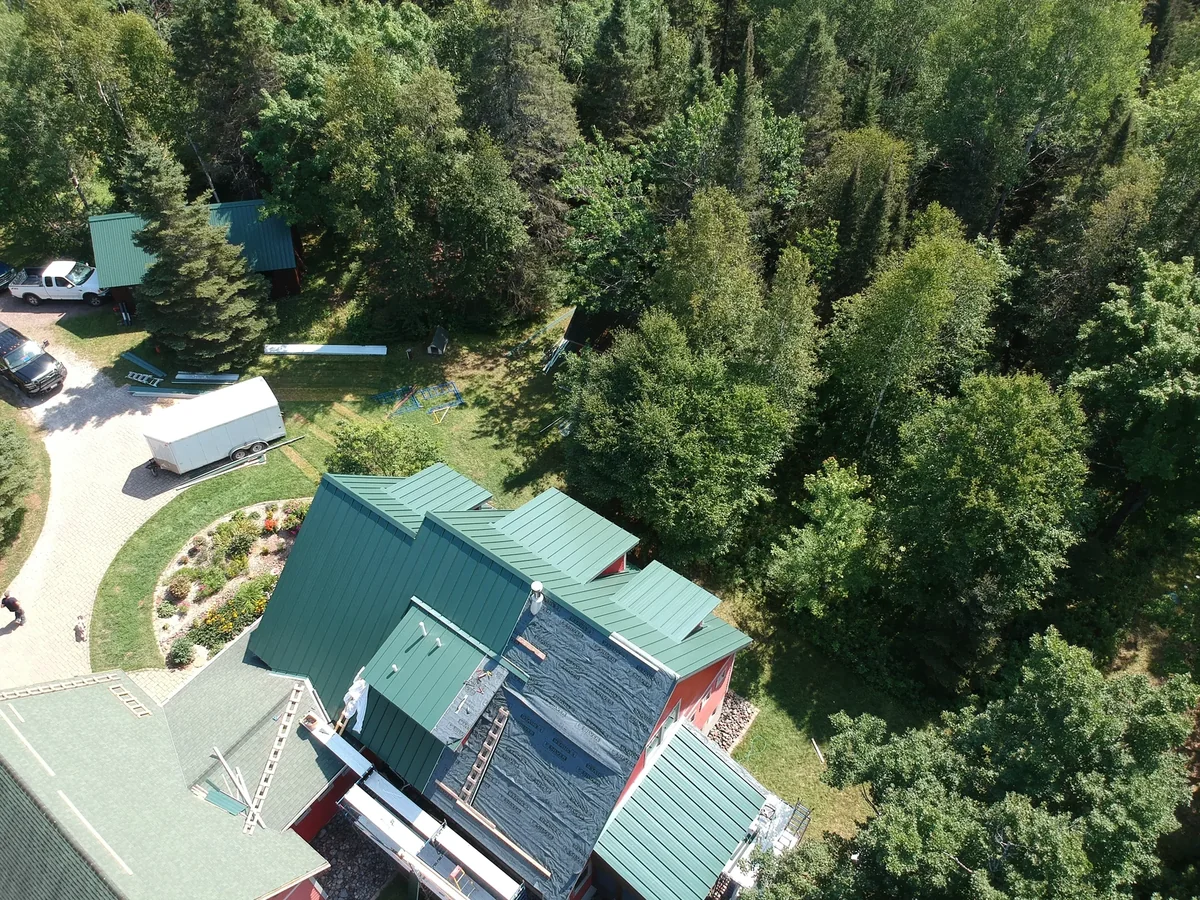 Aerial view of an evergreen standing seam metal roof on a red home tucked into wooded grounds near Duluth, MN