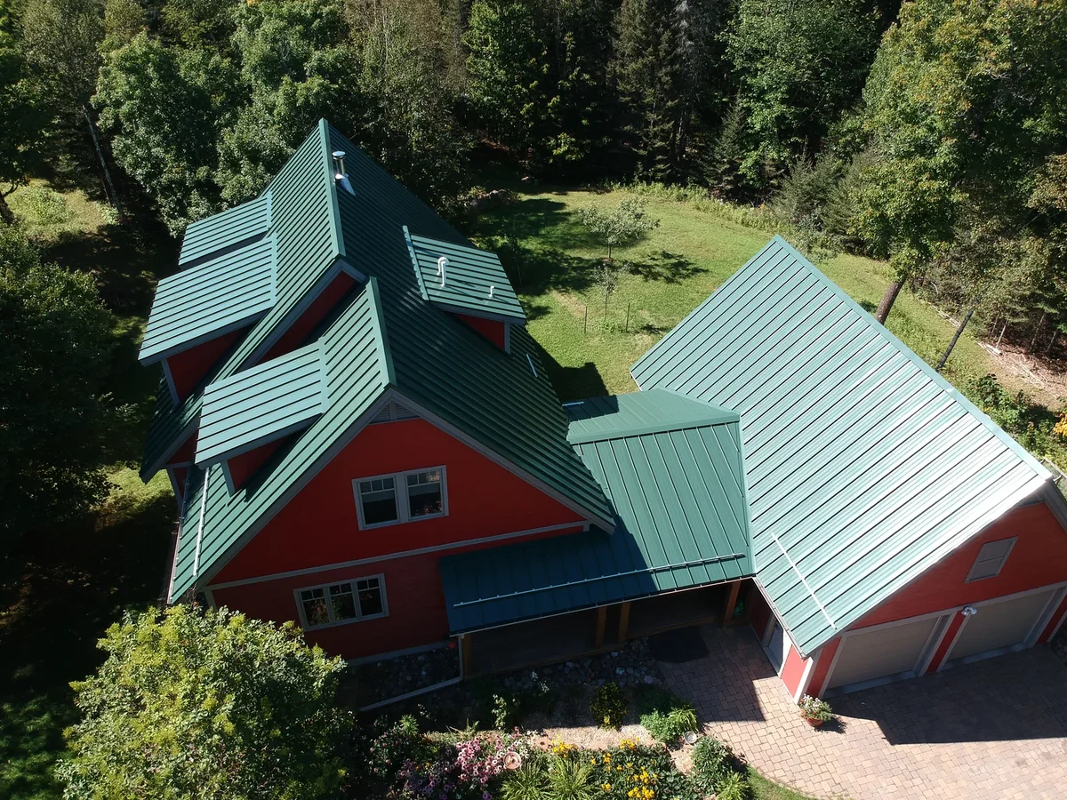 Lower-angle look at the dark green metal roof above the paver entry and garden beds