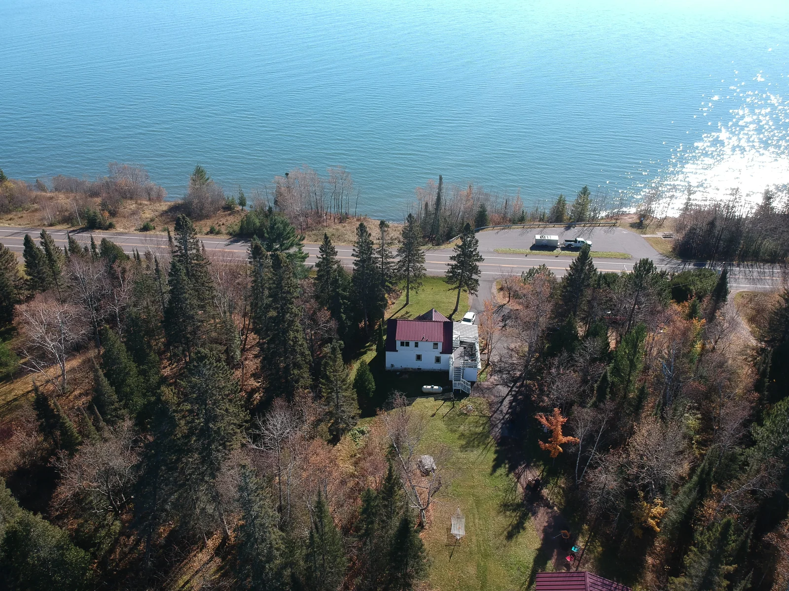 Wide aerial of a white home with a deep red standing seam metal roof overlooking Lake Superior in Duluth, MN.