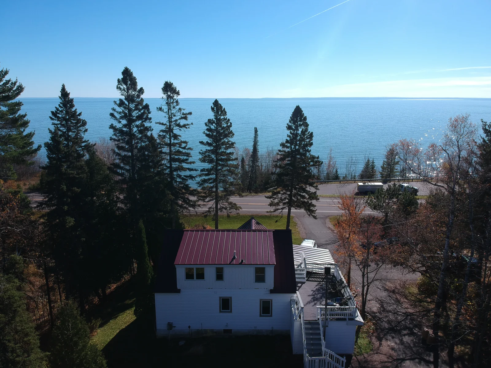 Elevated view of the white house and red metal roof set among evergreens with the blue lake on the horizon.