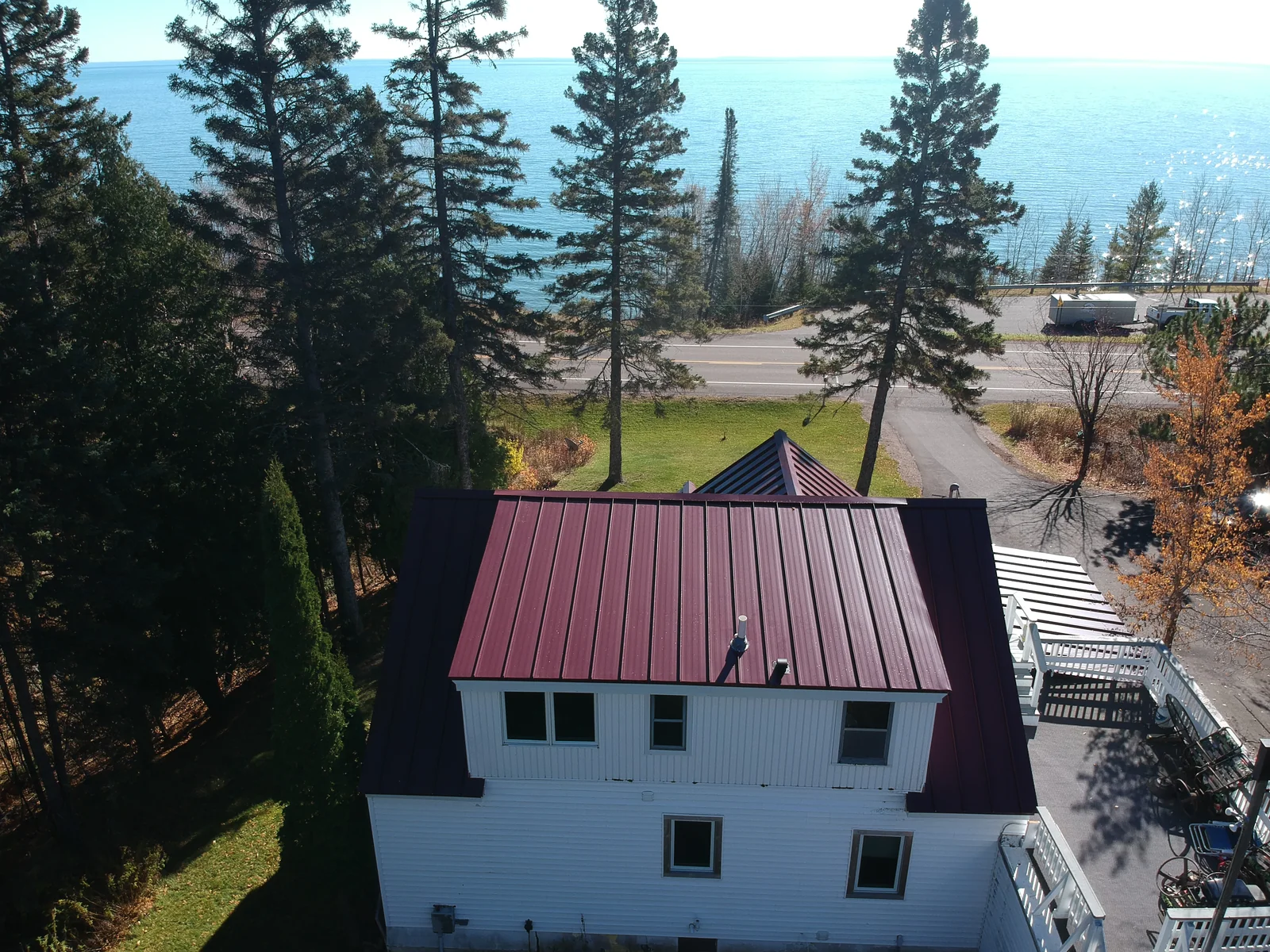 Gable end of the white home crowned by the red metal roof with the lake stretching behind it.