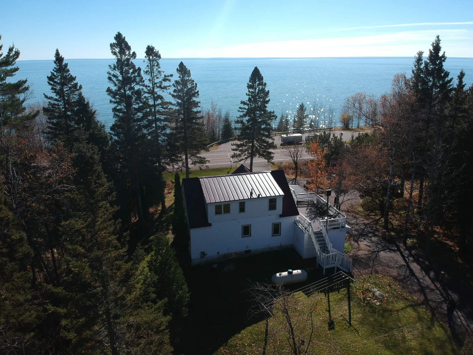 Side angle of the red metal roof and white siding with the shoreline visible beyond the trees.