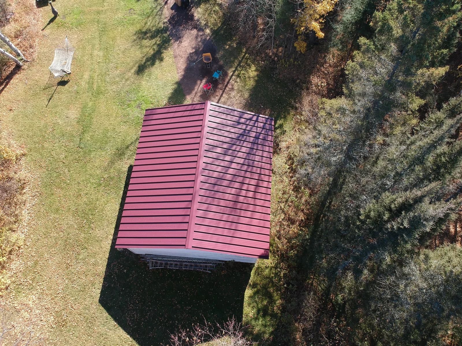 Red standing seam roof above a green lawn, framed by bare trees and brush.