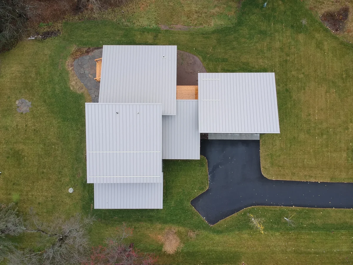 Top-down drone shot of the contemporary home's white metal roof planes and angular layout.