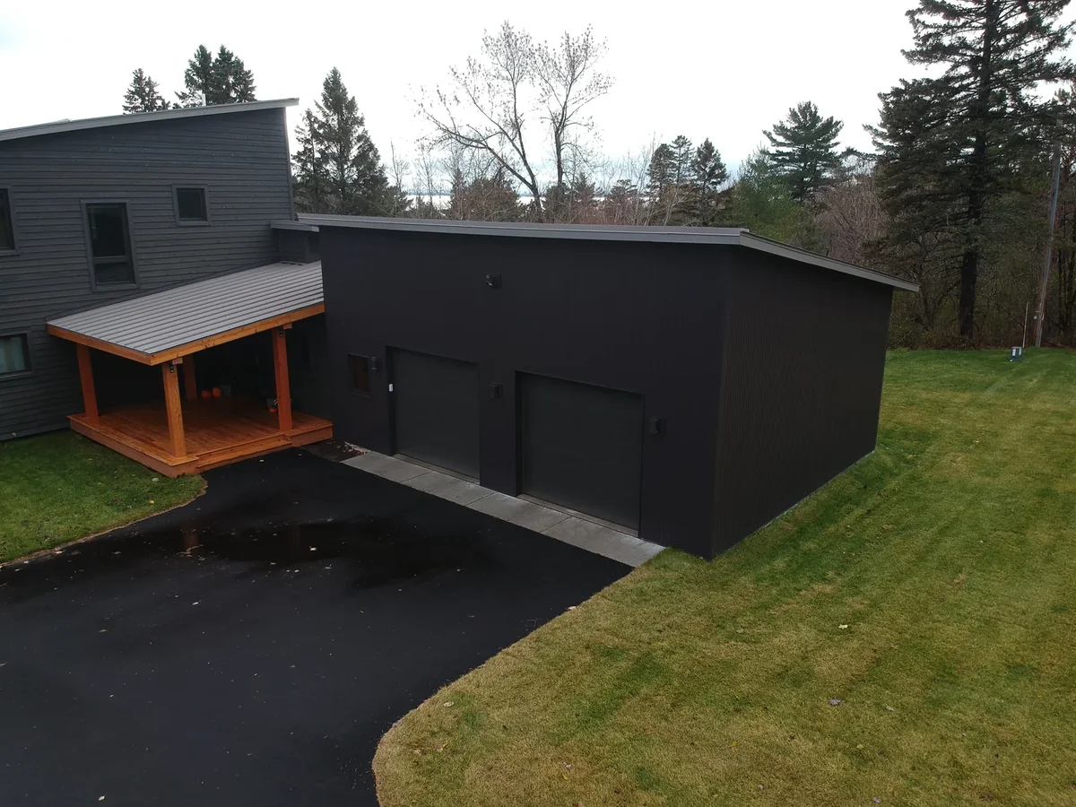 Side view of the dark-clad garage wing with its low-slope metal roof and timber carport.