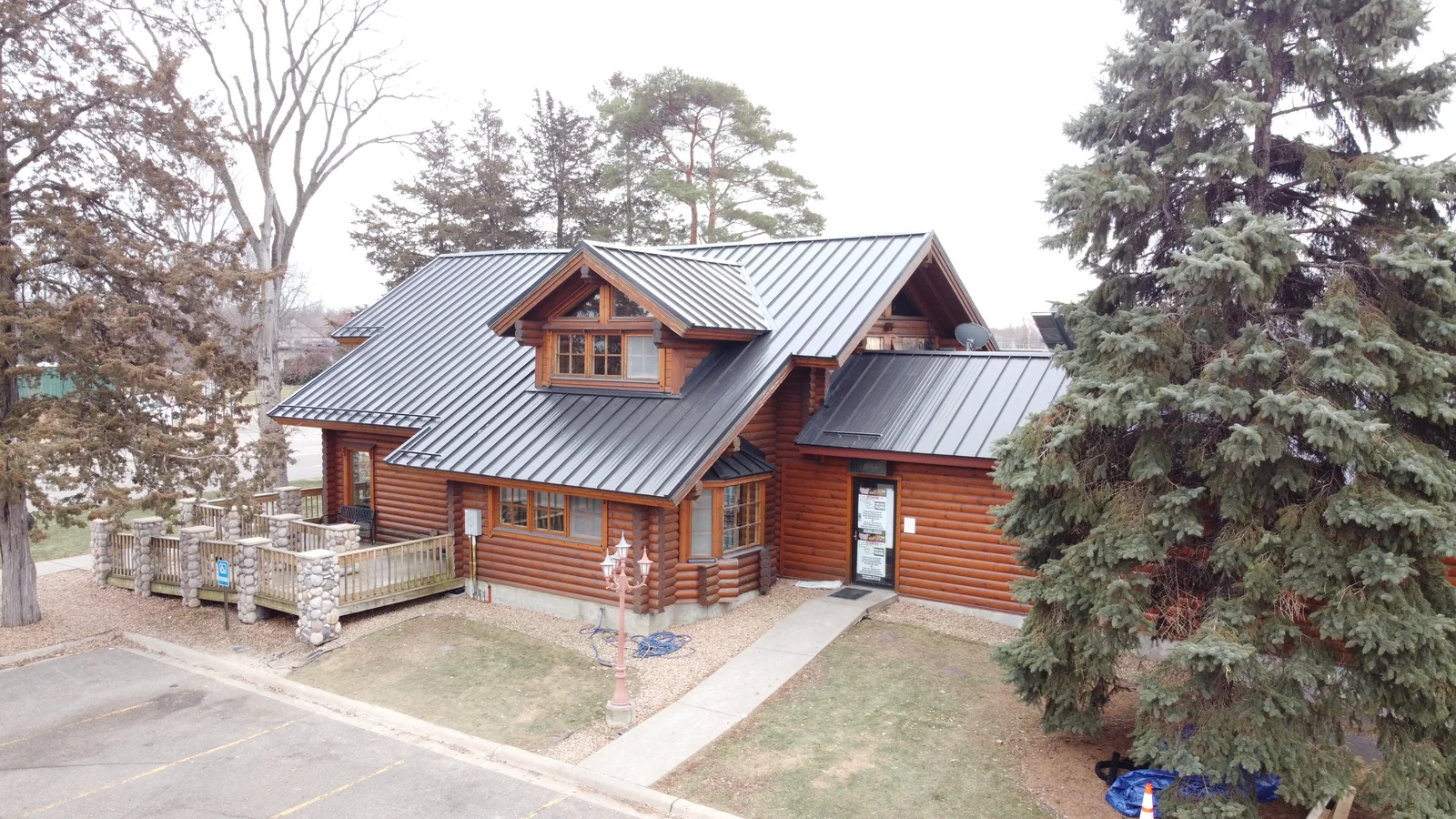 Drone angle of the timber building's multi-gable gray metal roof framed by tall evergreens