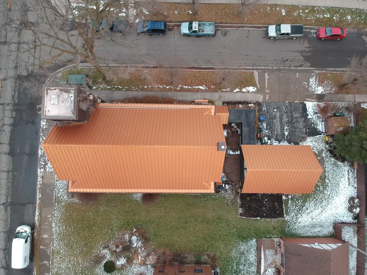 Aerial view of a long copper-toned standing seam roof on a large brick building in Eau Claire, WI, with snow dusting the surrounding streets.