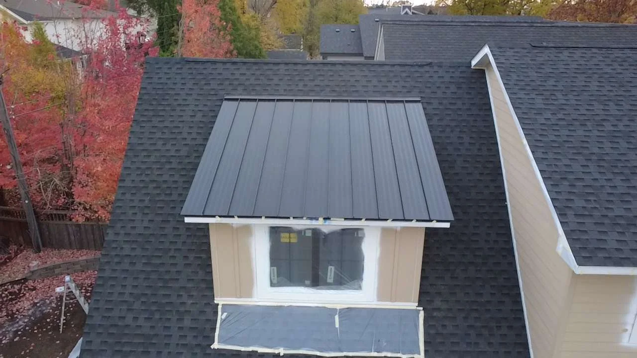 Black standing seam metal roof crowning a dormer cupola above tan lap siding