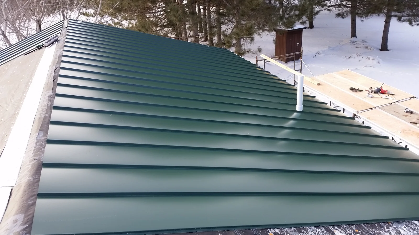 Close-up of the green standing seam panels and ridge running down the snow-dusted roof.