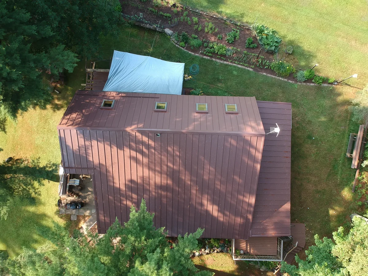Overhead drone shot of the brown screw-down metal roof on the home surrounded by green lawn