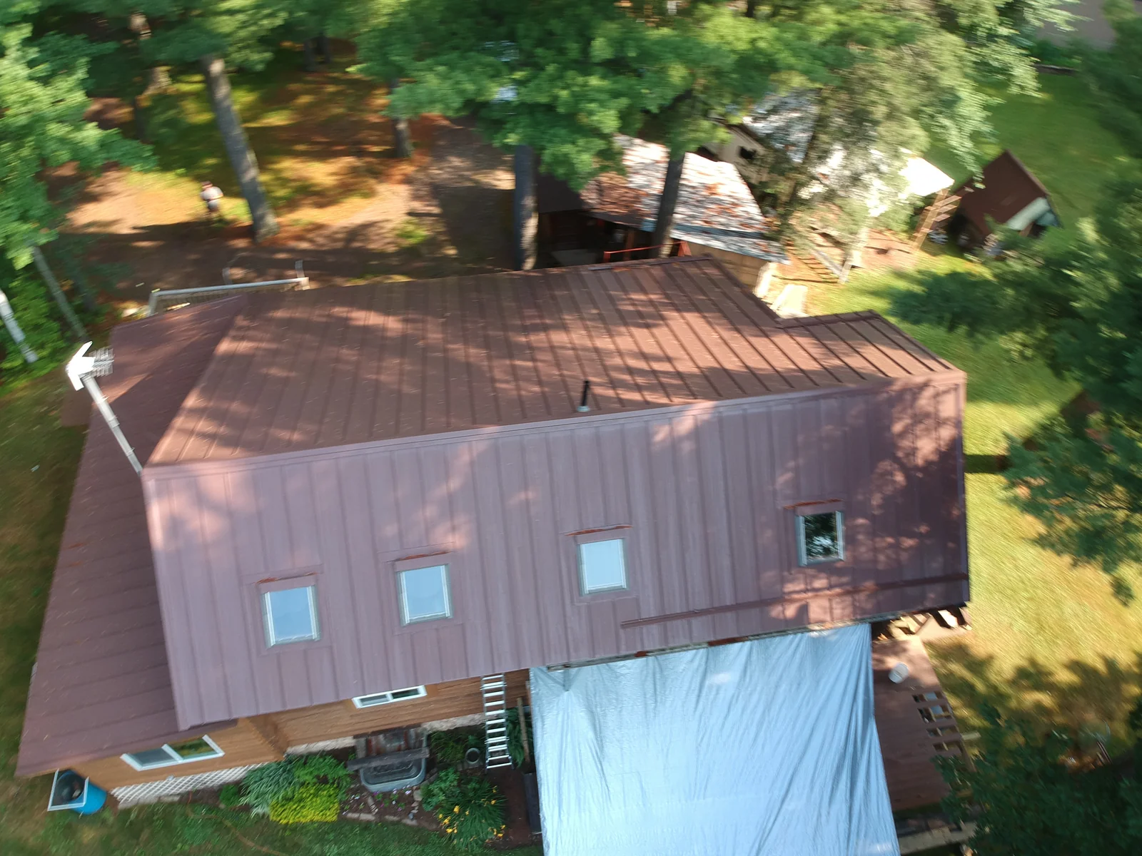 Drone view across the brown metal roofline showing the home and detached structures