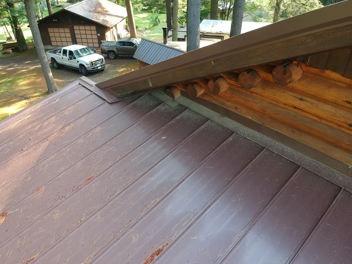 Detail of the brown metal roof slope meeting the wood-trimmed eave