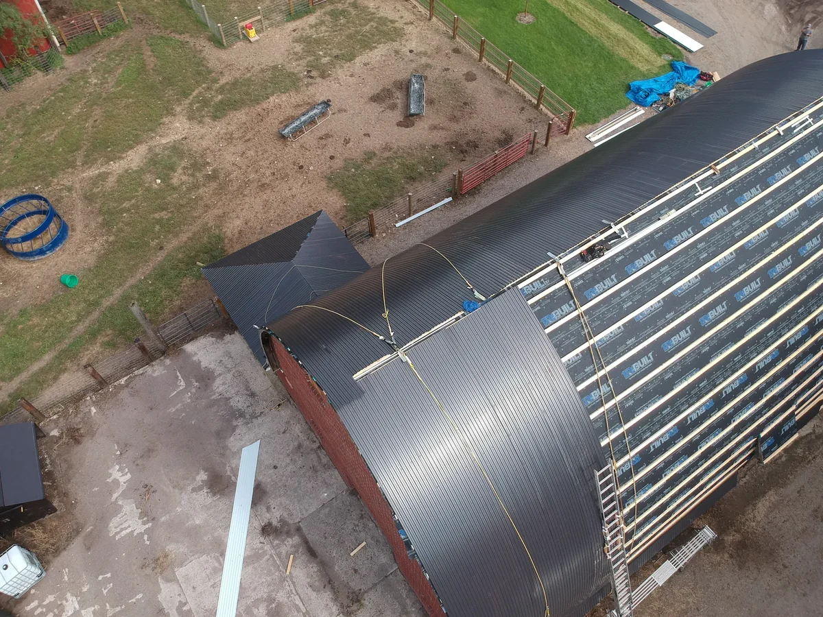 Detail of the barn's red brick gable end and stone foundation below the new roof