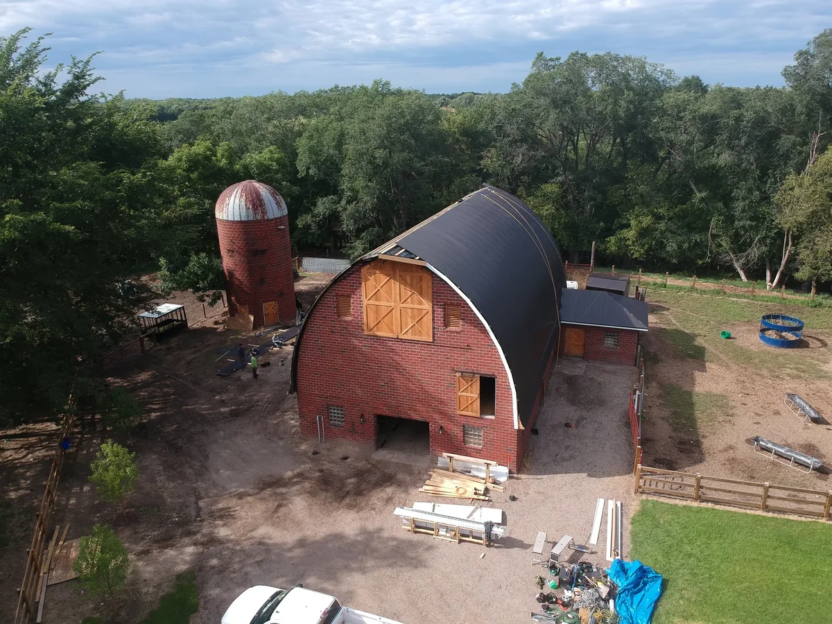 Ground-level angle of the curved-roof barn flanked by two silos and red brick walls