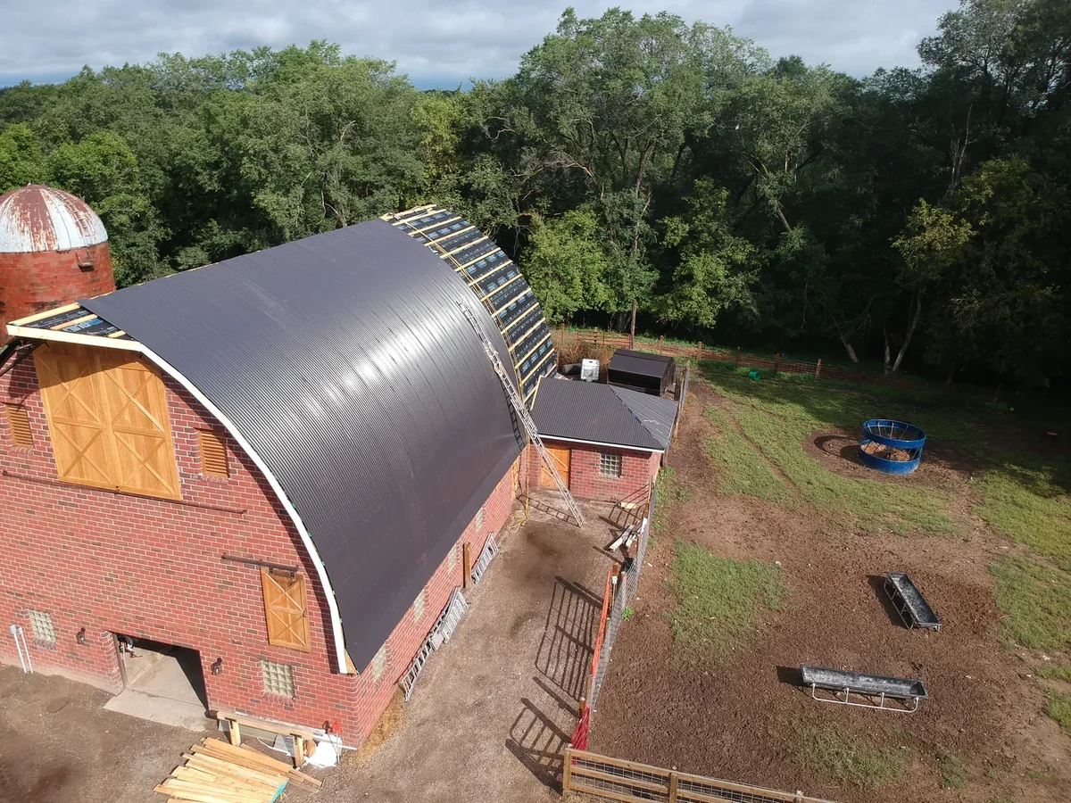 Drone view of the dark metal-roofed barn and silo surrounded by autumn-tinged trees