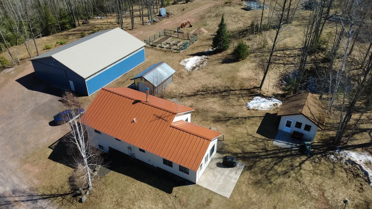 The rust-orange metal roof beside a blue pole barn outbuilding across the property