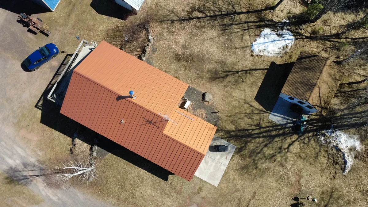 Overhead look at the orange roof beside the gravel drive and parked vehicle