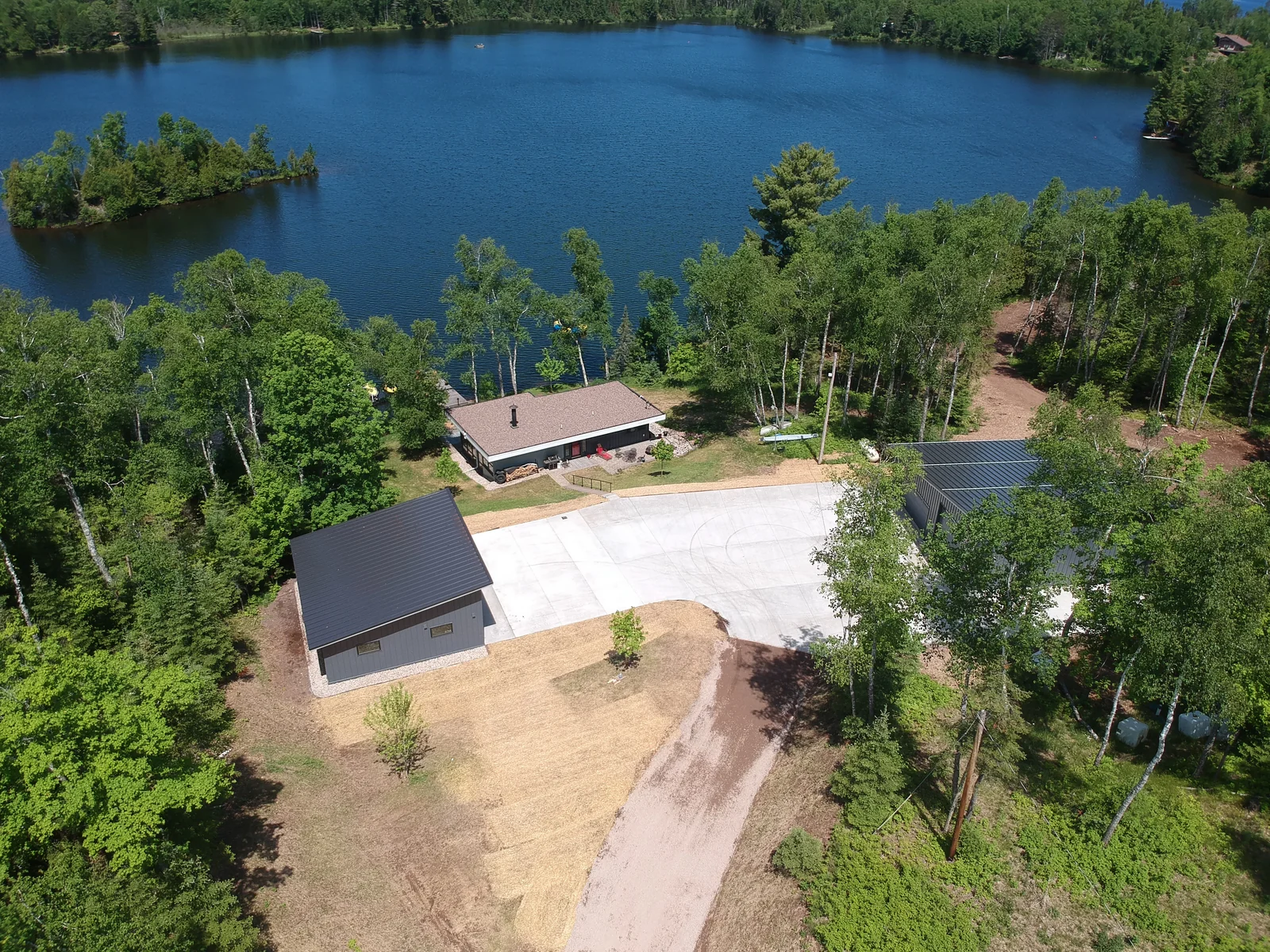 Sweeping aerial of a modern black metal-roofed cabin beside a forest-rimmed lake near Grand Marais, MN.