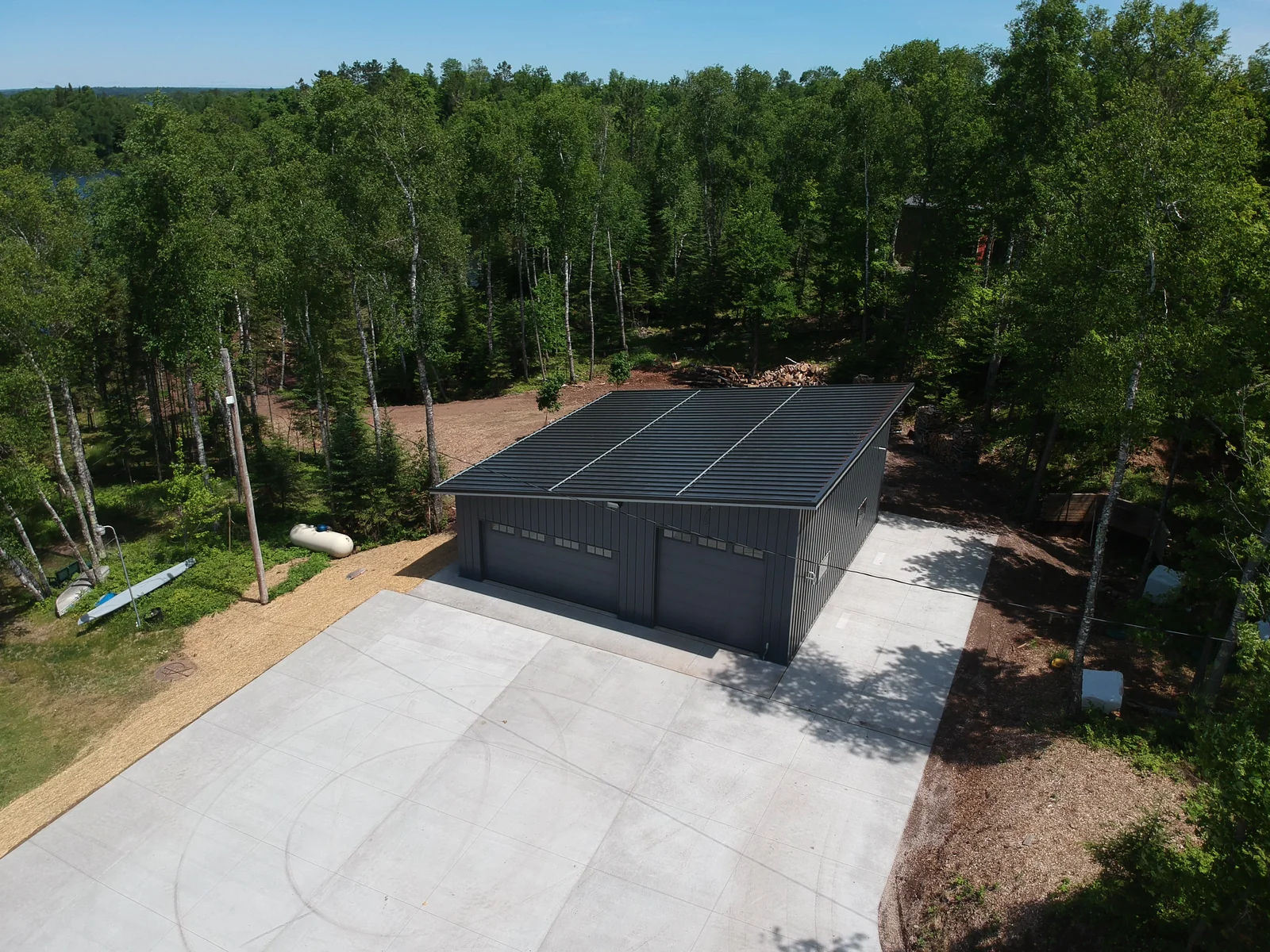 Side view of the dark standing seam roof and the broad concrete apron leading to the garage.