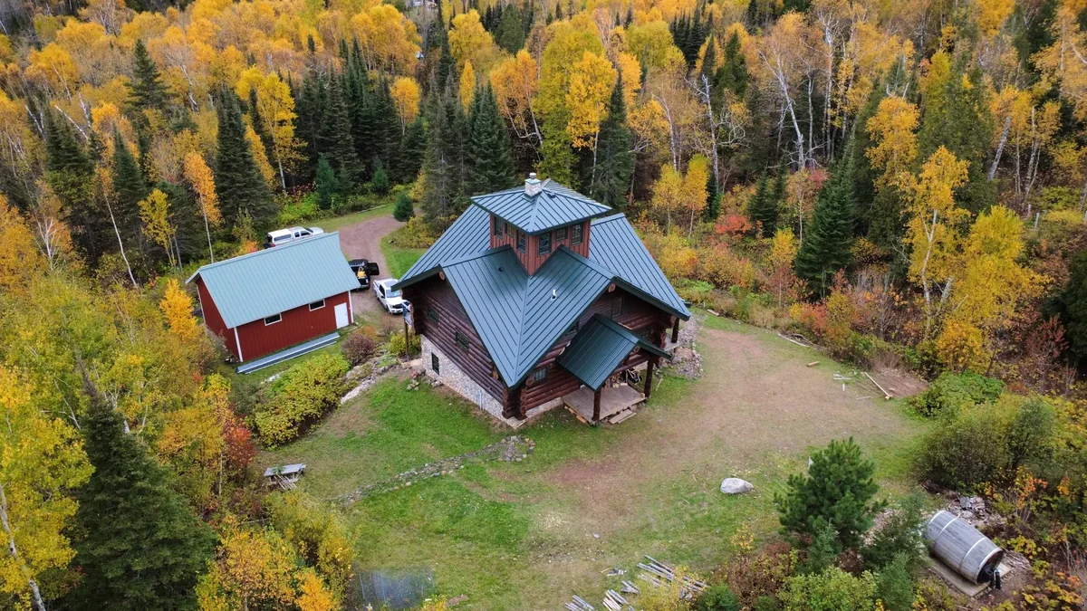 Angled aerial of the grey metal roof with a red outbuilding in the clearing nearby