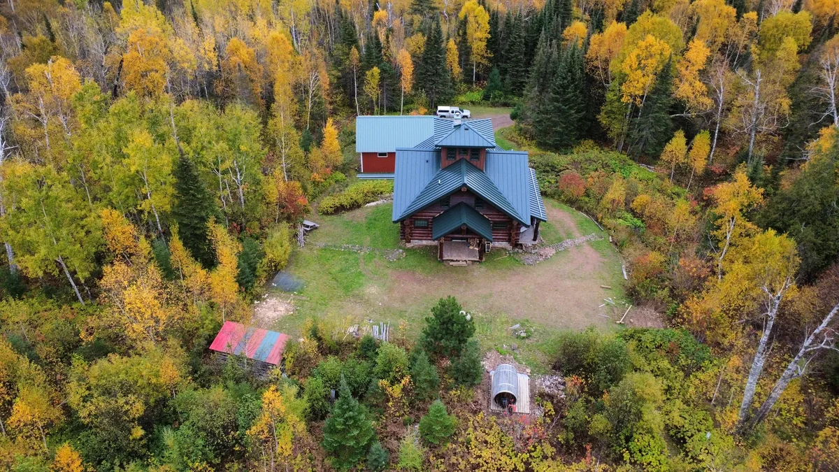 High wide shot of the lodge tucked into the forest with the grey roof visible below