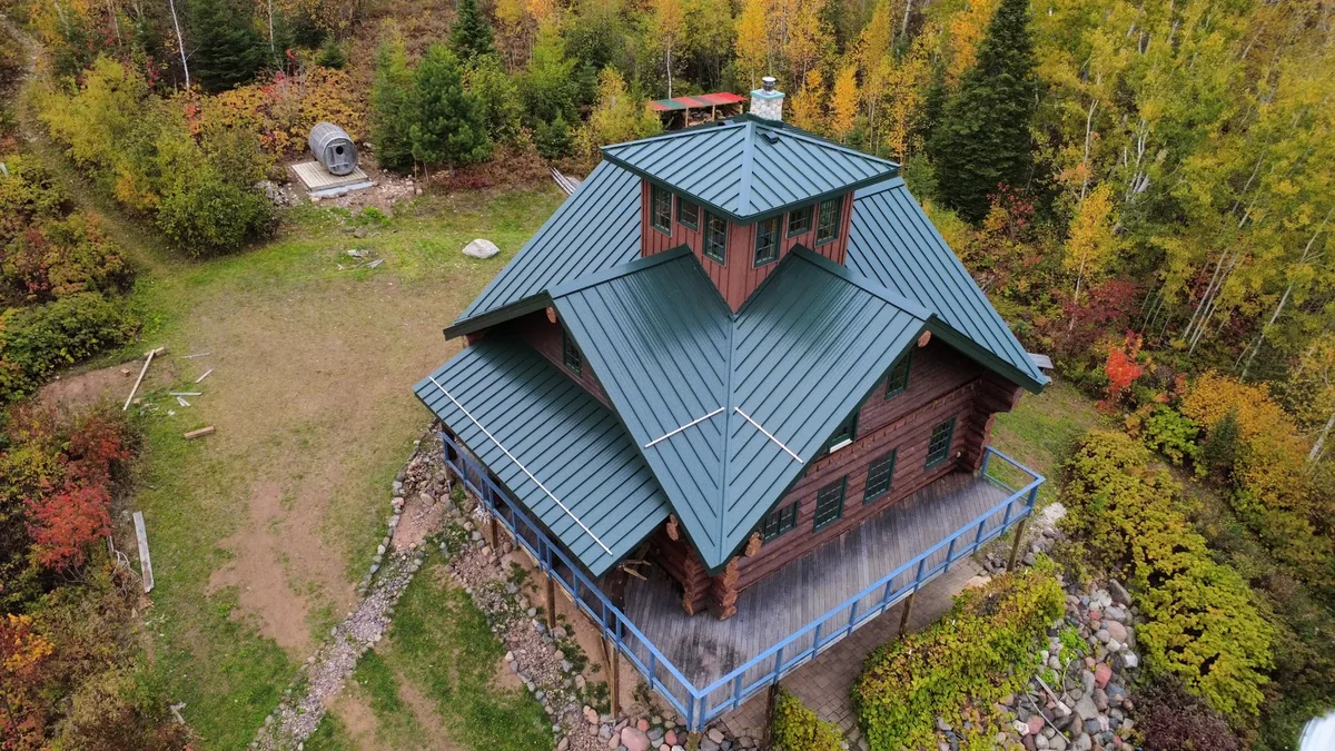 Distant aerial showing the log lodge and grey roof among the rolling autumn landscape