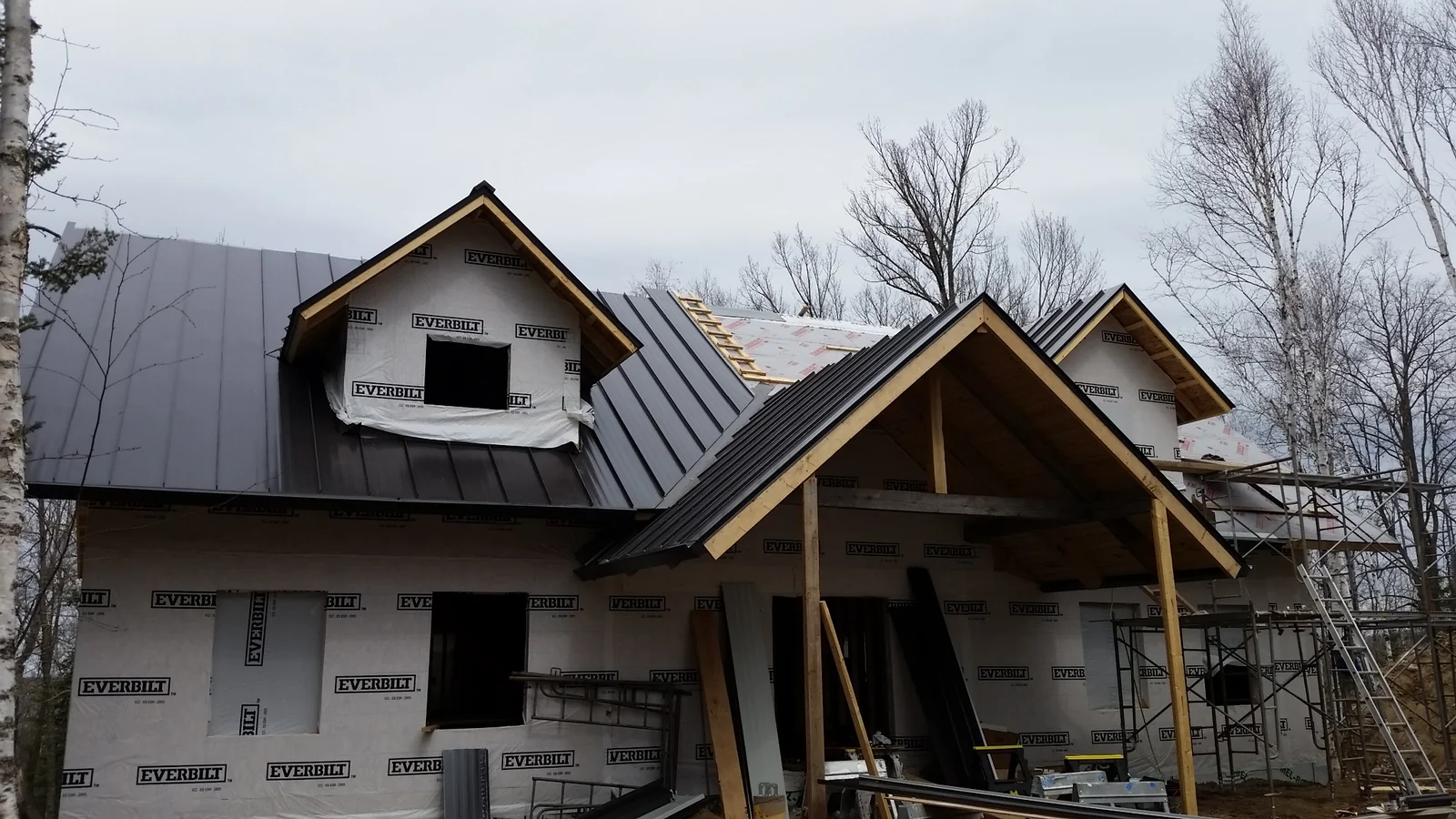 Mid-build view of the charcoal metal roof going on over housewrap and exposed framing