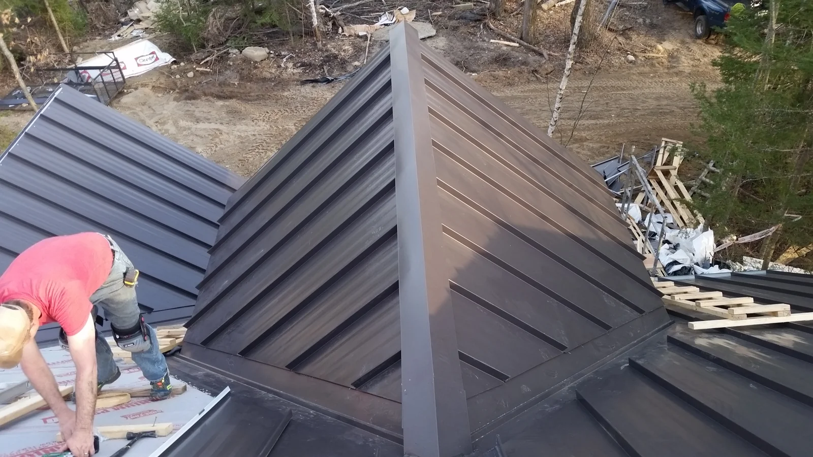 Close detail of a roofer working on the gray standing seam panels at the hip