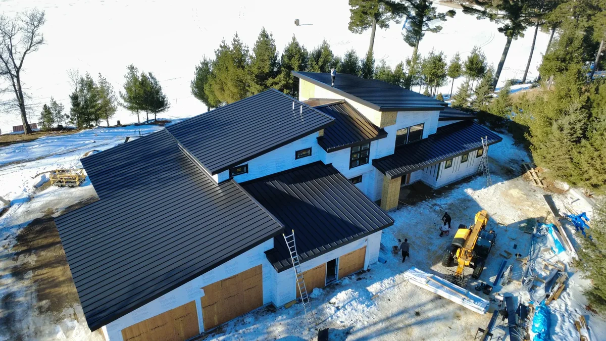 Low aerial angle showing the dark standing seam panels and exposed framing of the build site.