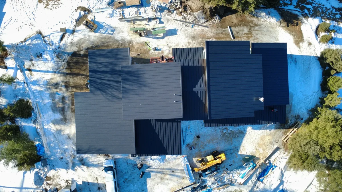 Overhead view of the matte black metal roof with construction equipment in the snowy yard.